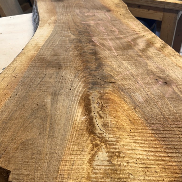 One rough-sawn live edge black walnut slab laid flat on the bench, the grain and edge visible before anything is cut.